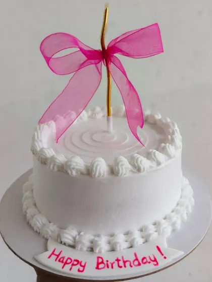 A simple and elegant cake with a single pink ribbon tied around a candle, perfect for a minimalist celebration.
