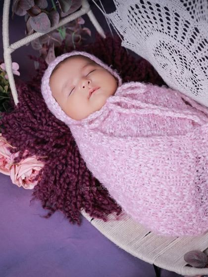 Another angle of the purple floral swing, showing the baby swaddled and sleeping soundly.