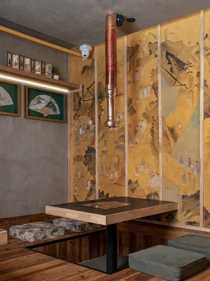 This traditional floor seating area features a striking yellow canvas wall inspired by layered Korean paintings. The custom copper chimney is a functional necessity for in-table grilling that we designed as a sculptural element, blending utility with aesthetic grace.