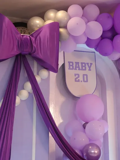 A close-up of the statement purple bow, the centerpiece of this modern baby shower theme. The fabric and structure add a touch of drama and elegance to the backdrop.