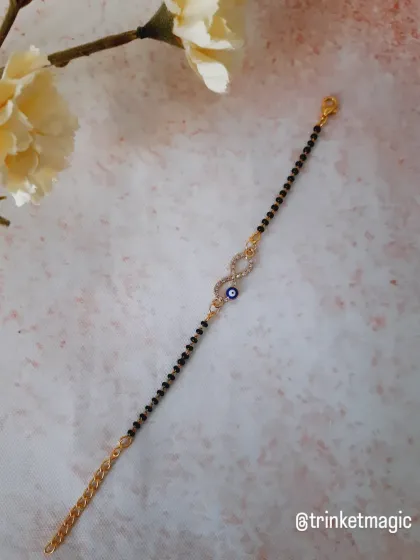 A full view of the infinity evil eye mangalsutra bracelet. The gold-plated chain and classic black beads make it a timeless piece.
