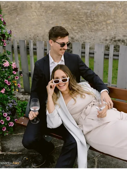 Relaxing on a bench with wine, sunglasses, and big smiles. This portrait is effortlessly cool and full of personality, capturing a moment of fun during their Swiss engagement shoot.