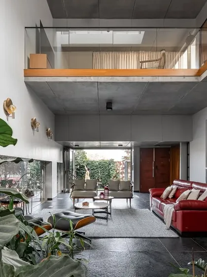 This is the heart of our project, 'Roots'. We designed this double-height living space to dissolve the boundaries between inside and out. The raw concrete ceiling and Cuddapah stone floor are balanced by the warmth of wood and the vibrant red sofa, creating a space that feels both expansive and inviting, with greenery flowing in from the garden.