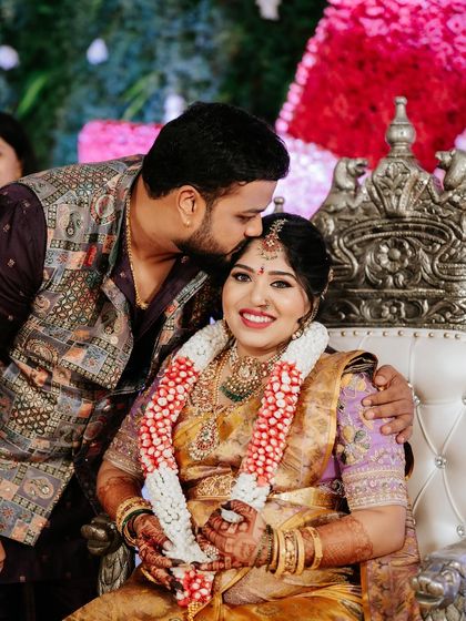 A beautiful moment from a baby shower. The mother-to-be is radiant in a yellow and lavender saree, while the father-to-be kisses her forehead, dressed in a complementary embroidered vest.