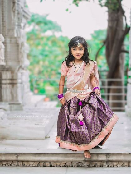 This little girl looks like a princess in her traditional dress, walking down the steps of a temple-like structure during her Vara Mahalakshmi festive shoot.
