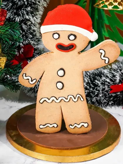 A giant, cheerful gingerbread man cookie presented as a Christmas showpiece. The festive background with a Christmas tree makes it a fun and iconic holiday image.