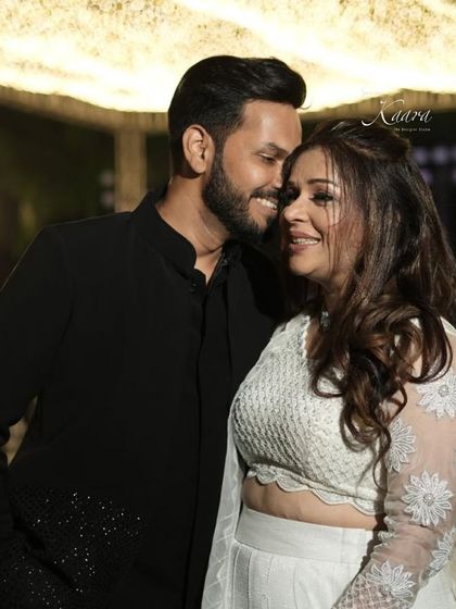 A candid shot of a couple sharing a happy moment. Her white lehenga with sheer embroidered sleeves and his sharp black kurta were designed by us for a coordinated, elegant look.