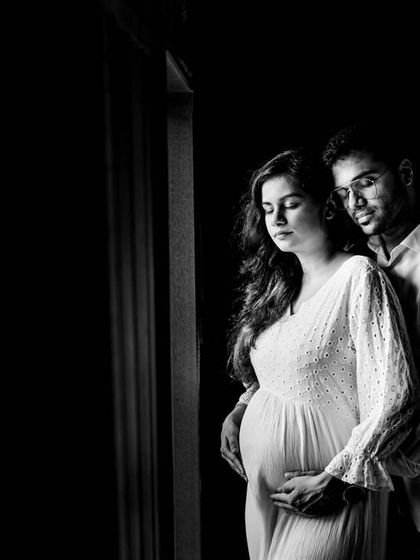 An intimate black and white maternity portrait of a couple. The soft window light and close embrace create a feeling of warmth and anticipation as they await their new arrival.