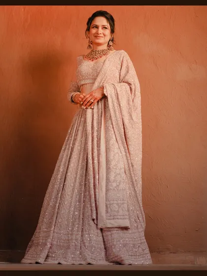 A classic, full-length studio-style portrait of the bride. The warm lighting enhances the rich texture and color of her beautiful engagement lehenga.