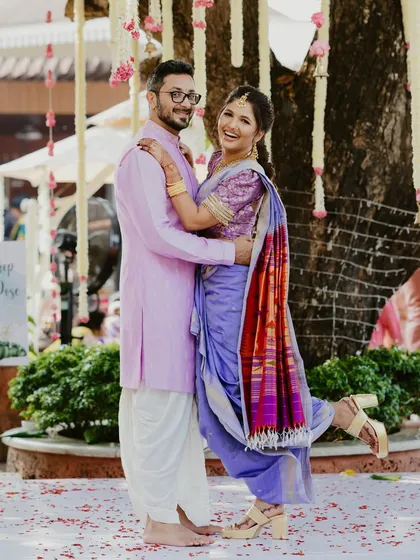 A joyful Maharashtrian couple poses for the camera, with the bride kicking up her heel in a fun, candid moment that shows their vibrant energy.