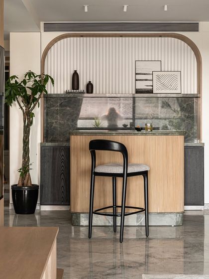 A full view of the arched bar in the Noir Blanc House, featuring a sage green marble top, warm oakwood flutes, and a black veneered cabinetry for a look of minimal, quiet luxury.