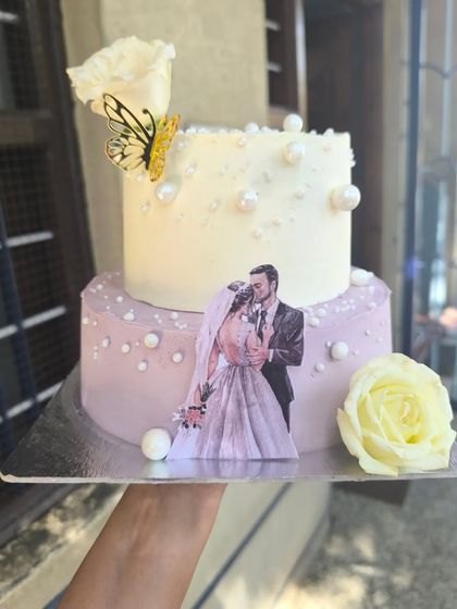 A personal and romantic two-tier anniversary cake. This design features a lovely edible print of the couple, delicate sugar pearls, and a handmade sugar flower for a truly custom touch.