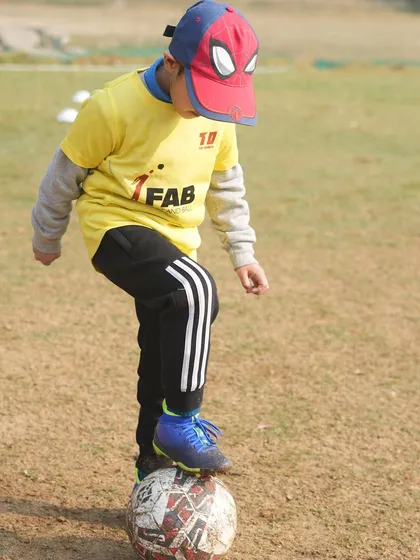 A young player in a Spiderman cap with his foot on the ball. We foster a love for the game by making it fun, which is key to building determination and discipline.