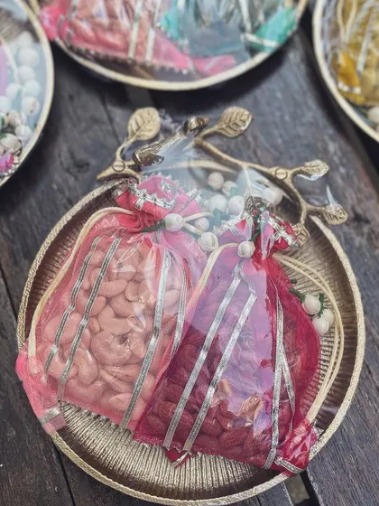 Two vibrant red potlis filled with cashews, nestled on a dull gold platter. This detail from the "Jashn" series shows how I balance rich colors with elegant, understated containers.