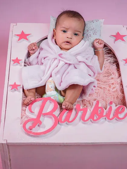 An awake baby in the Barbie box prop, looking right at the camera.