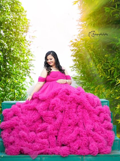 A stunning shot of a mother-to-be in a vibrant pink ruffled gown, seated on green steps in our garden.
