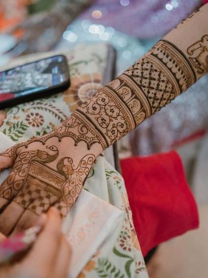 An in-progress shot, showing the artist's phone displaying the reference design while creating the intricate pattern on the client's arm.