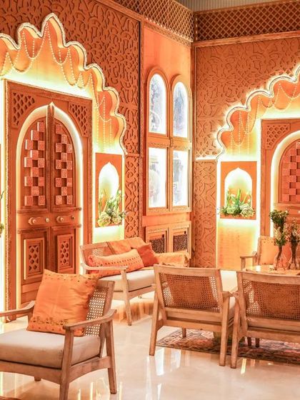 The lounge area for the Graha Shanti Puja, with custom-designed furniture and intricate jaali work on the walls, all bathed in a warm, inviting light.