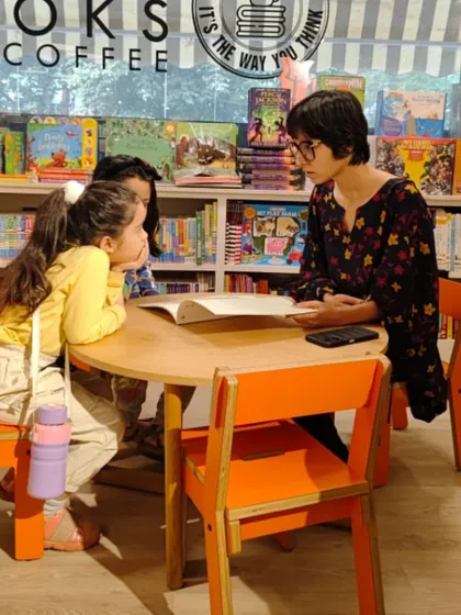 A storyteller engaging with two young listeners at a small table. These smaller, more personal interactions during our sessions help ensure every child feels included in the story.