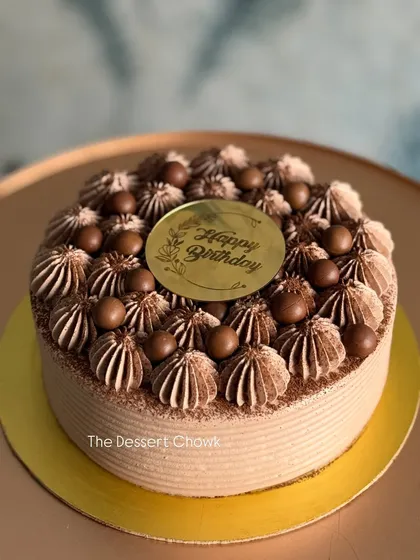 A rich chocolate cake topped with chocolate cream swirls and crispy chocolate balls.