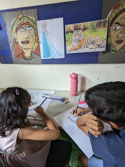 Students working side-by-side, using reference pictures of tigers and cultural figures to guide their drawings.