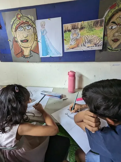 Students working side-by-side, using reference pictures of tigers and cultural figures to guide their drawings.