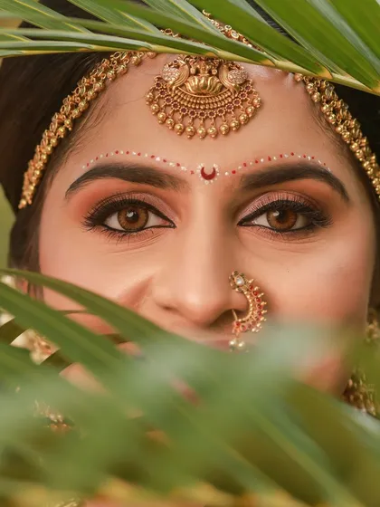 A peeking shot through palm leaves, this portrait is playful and intimate, capturing the bride's beautiful eyes and traditional matha patti.