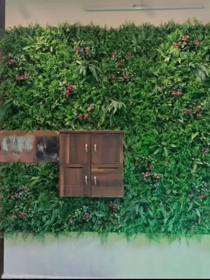 A premium artificial green wall installed in the porch area of a private bungalow. This design incorporates a variety of textures and subtle color variations to mimic a natural vertical garden and seamlessly integrates a wooden utility box.