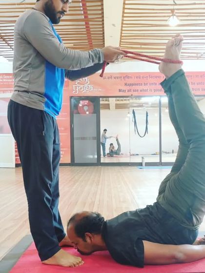 I am helping a student work on a deep leg and back stretch using a strap. This kind of partner assistance can help release tension and improve flexibility.