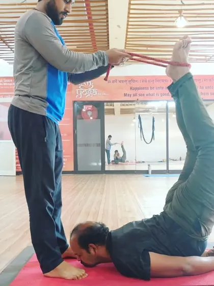 I am helping a student work on a deep leg and back stretch using a strap. This kind of partner assistance can help release tension and improve flexibility.
