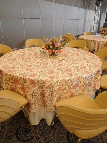 Elegant guest seating for a daytime luncheon. The round tables are covered with floral-patterned tablecloths and surrounded by comfortable, modern chairs, with a beautiful centerpiece to complete the look.