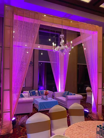 An indoor lounge area for a wedding event, with comfortable sofas set under a simple canopy with a chandelier. Perfect for guests to relax.