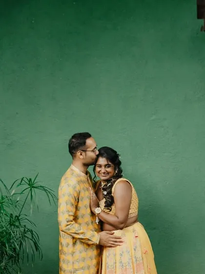 A candid moment from a haldi ceremony, with the couple sharing a happy, intimate moment against a vibrant green wall.