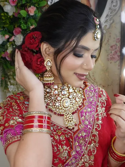 The model adjusting her hair, giving a better view of the red floral bun and the intricate details of her earrings.