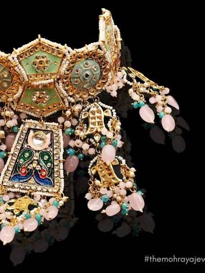 A close-up of a stunning meenakari choker with intricate peacock designs and pink and blue bead drops. A true piece of art.