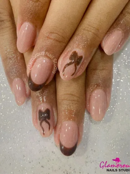 A chic and sweet design featuring a chocolate brown French tip on a nude base, with accent nails adorned with a cute, hand-painted brown bow.