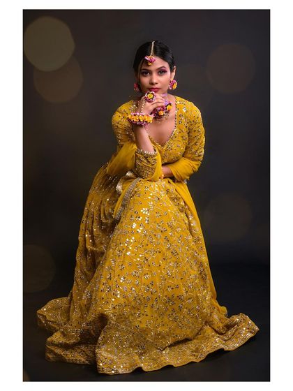 A full-length seated pose that shows the beautiful flare of the lehenga skirt. The dark background with bokeh lights adds a magical, celebratory feel.