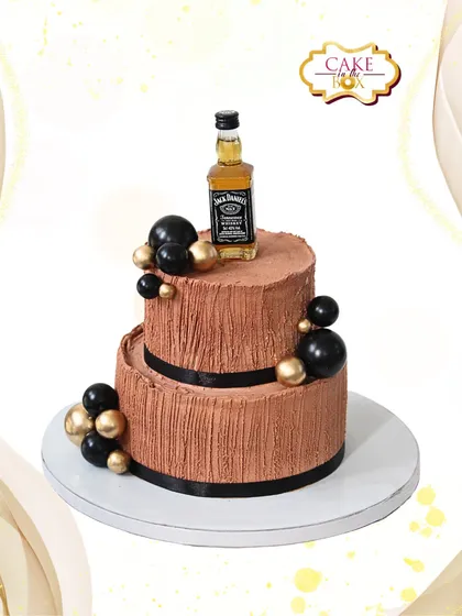 This two-tiered Jack Daniel's themed cake is perfect for celebrating a milestone with style. It features a rich chocolate texture, sophisticated black and gold accents, and is topped with a miniature bottle for a personalized touch.
