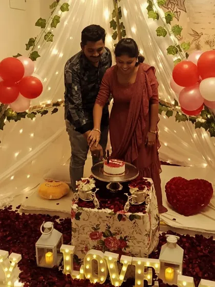 A happy couple cutting their anniversary cake inside a beautiful canopy tent I set up in their home, surrounded by rose petals, balloons, and 'LOVE' marquee letters.