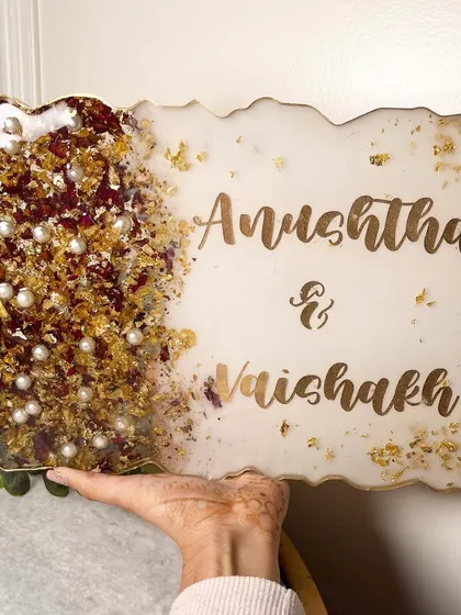 Turn your wedding garland into a beautiful nameplate for your home. This elegant piece features the couple's names in a beautiful script, with their preserved flowers, pearls, and gold flakes.