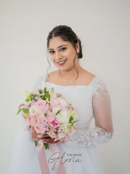 A classic bridal portrait of a Christian bride holding her beautiful bouquet of pink and white roses, looking directly at the camera with a warm smile.