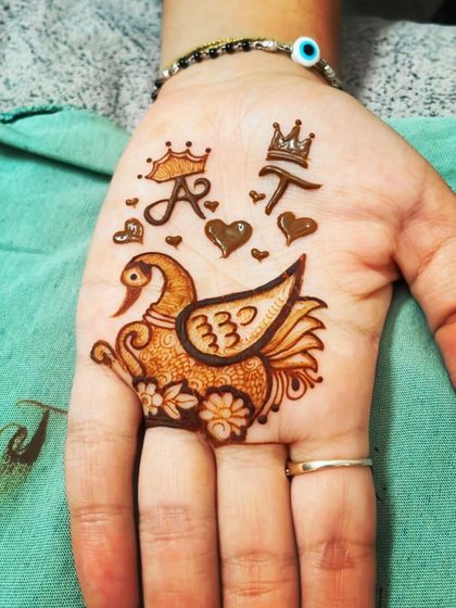 This design is full of personal symbols. It features the couple's initials 'A' and 'T' with crowns, hearts, and a beautifully detailed swan, telling a small story on the palm.
