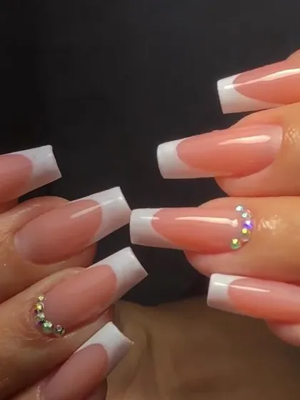 A classic French manicure on long square nails with two accent nails adorned with sparkling rhinestones at the base.