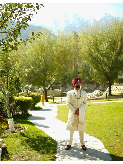 The groom, Rishi, standing in the lush gardens of the Manali wedding venue. The snow-capped mountains in the background add a majestic touch to this outdoor groom portrait.
