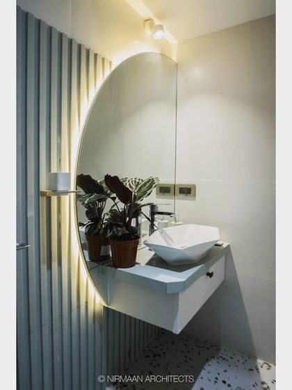 This bathroom combines terrazzo flooring with a fluted wall panel and a large, backlit circular mirror. The floating vanity adds to the modern, spacious feel.