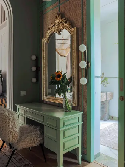 The master suite in 'Summer Haus' is a study in eclectic luxury. A mint green vanity and an ornate gold mirror create a sophisticated dressing area, with a doorway offering a glimpse into the stunning marble-clad bathroom.