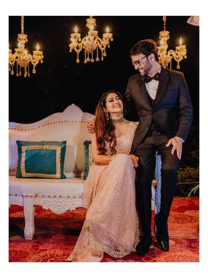 An elegant portrait of the couple at their Sangeet or reception, seated on a beautiful white couch.