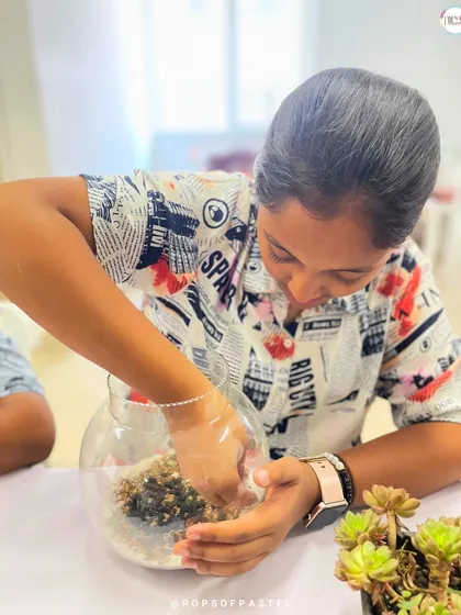 A young participant gets her hands in the soil, carefully arranging the base layer of her terrarium.
