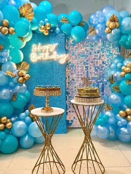 A stunning all-blue theme with a glittery blue backdrop. The scene is framed with a rich blue balloon garland accented with gold leaves, and features two elegant cake stands.