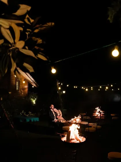 A wide shot of a couple enjoying a bonfire during their engagement celebration, with string lights creating a warm and cozy atmosphere.